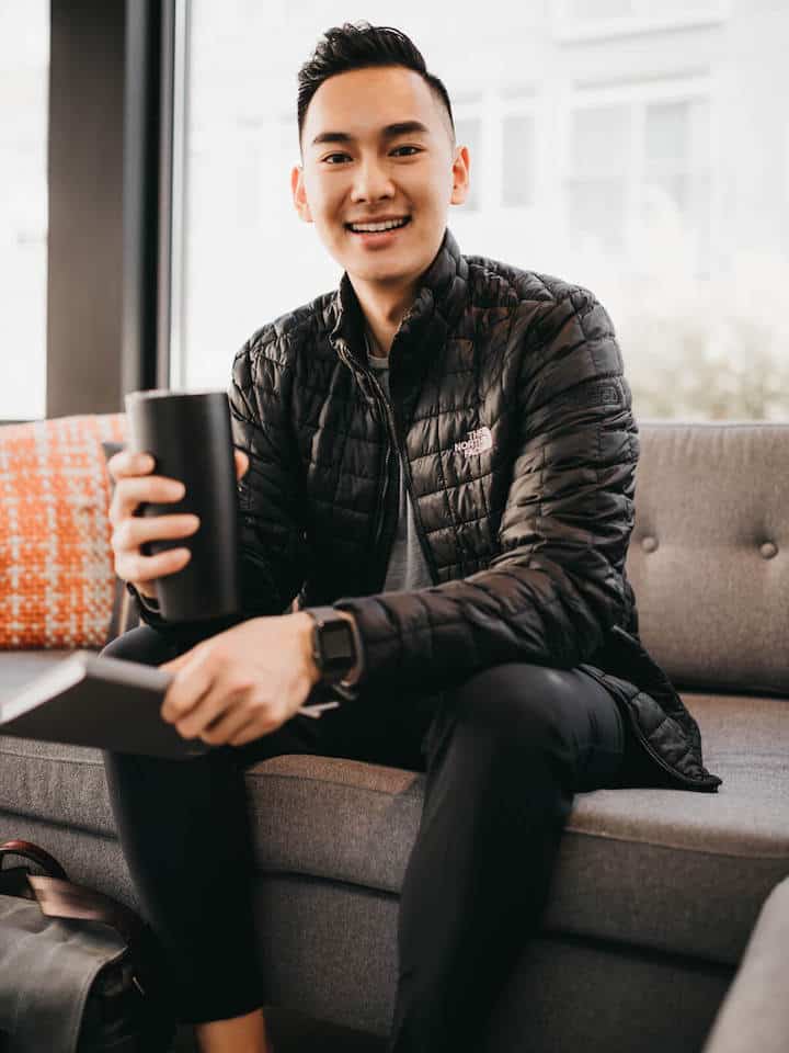 Man sitting down, holding a black mug, and smiling.