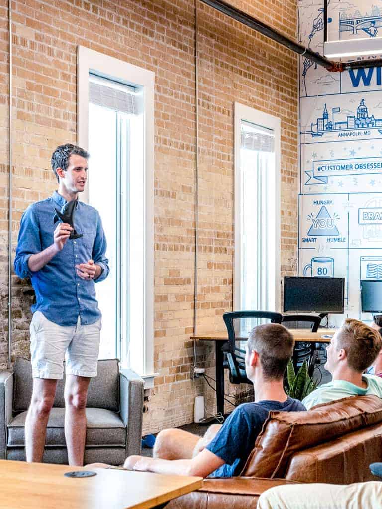 A man doing a speaking to three people seated on a couch.