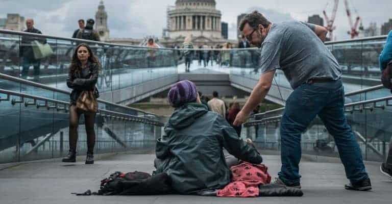 Person reaching hand out to another person sitting on the ground.