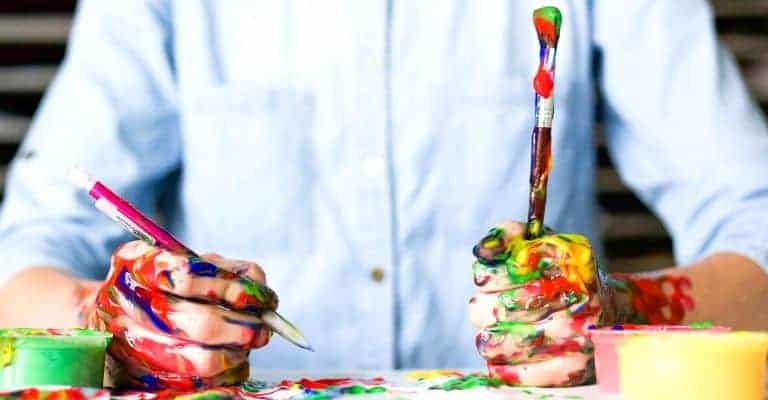 Close-up of hands holding a paint brush with paint splattered.