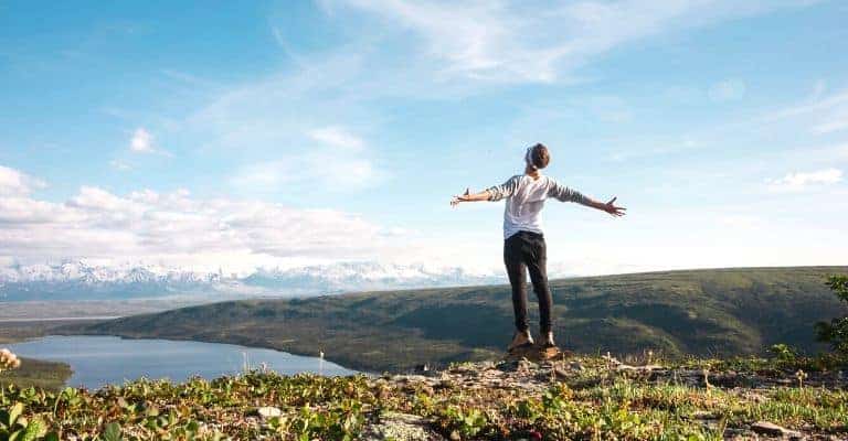 Person standing on cliff with arms up.