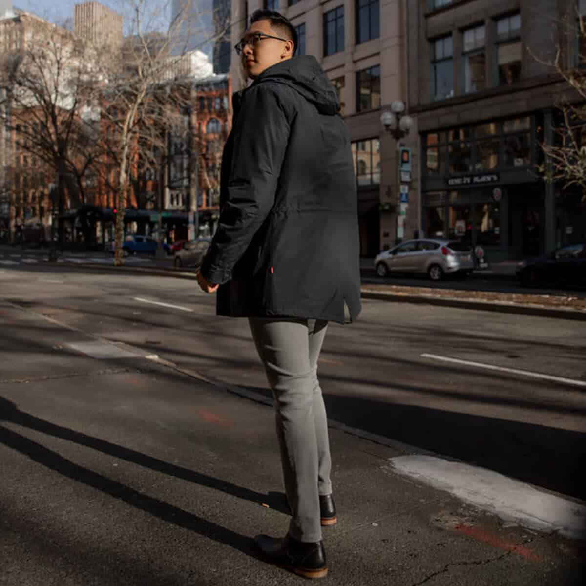 Man in grey jeans and rain coat walking.