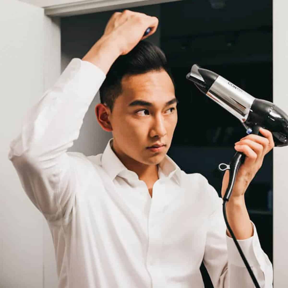 Person using a hair dryer and combing their hair.