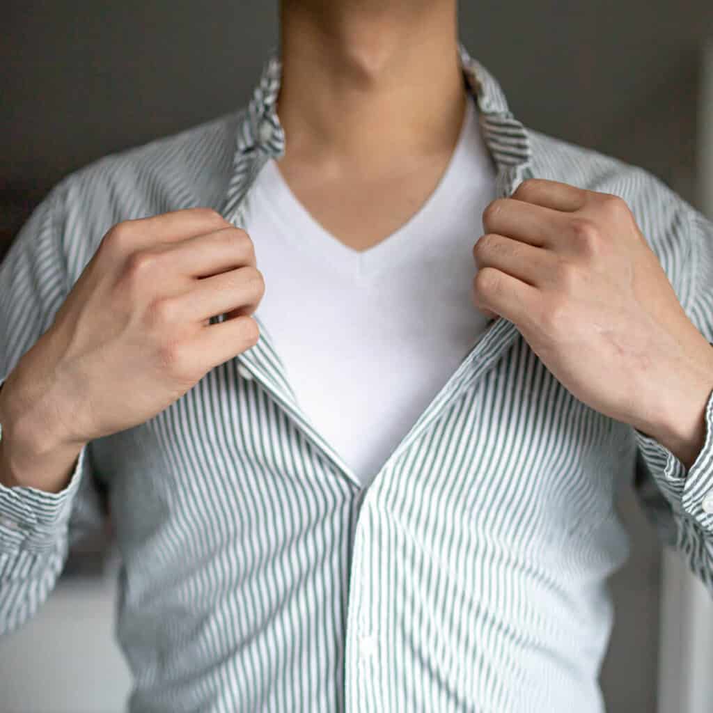 Person holding their shirt open to show their undershirt.