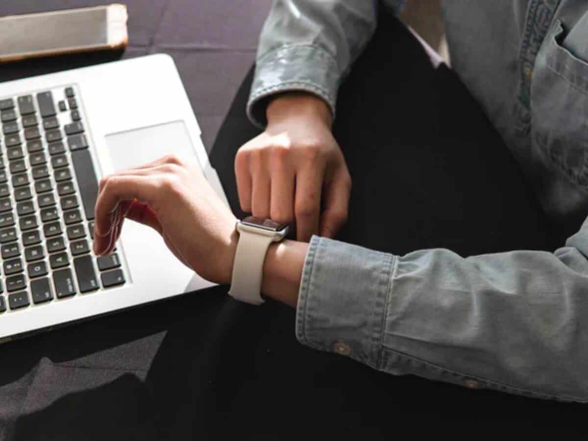 Person looking at their watch next to their laptop and phone.