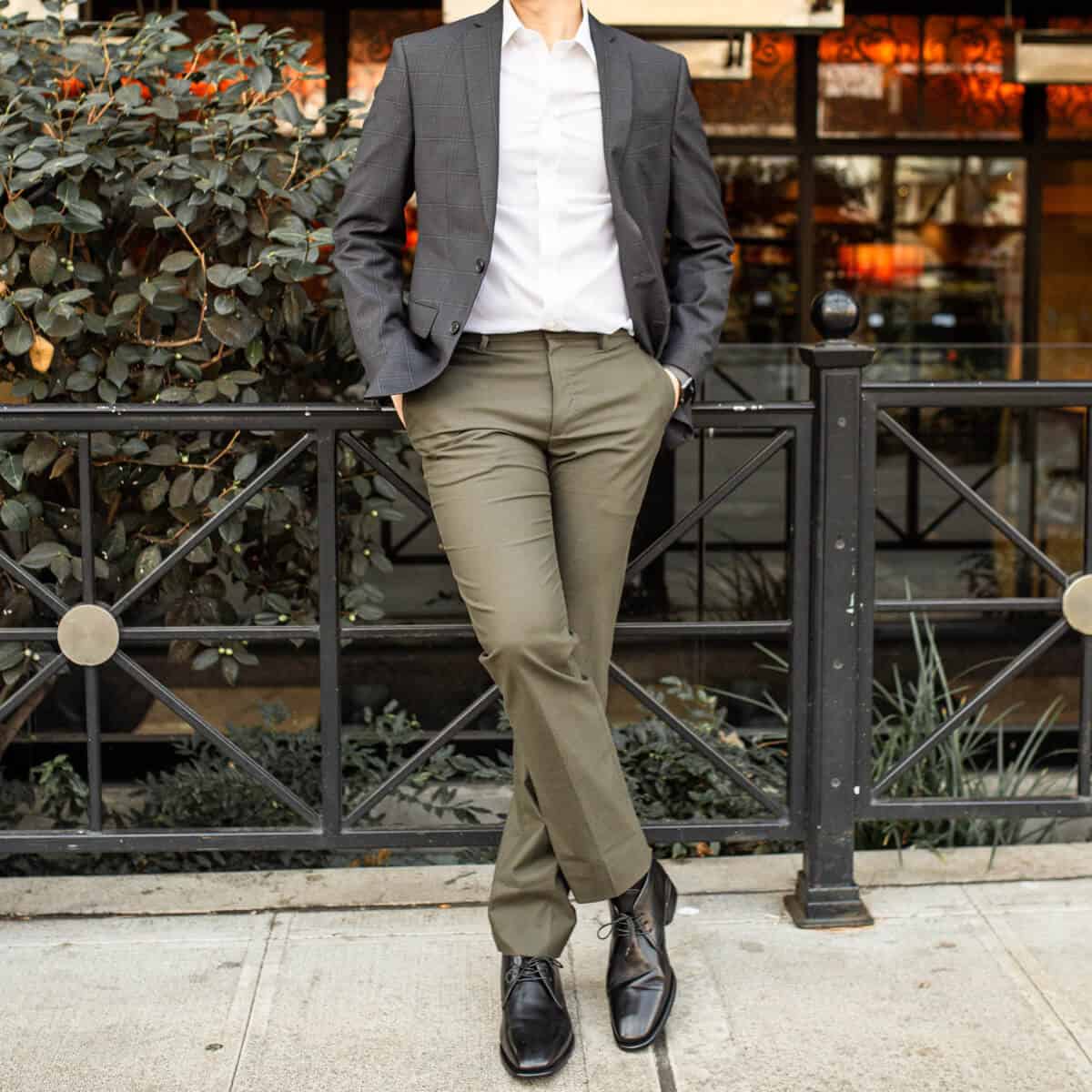 Neck-down of a person in green pants leaning against a railing.