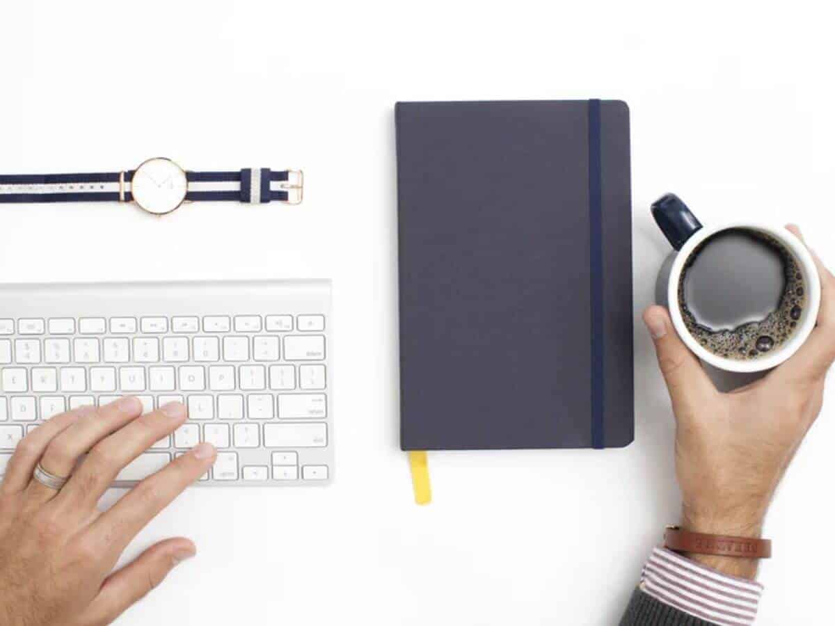 Person typing and holding a cup of coffee.