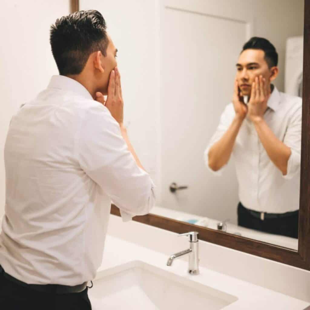 Person looking in the bathroom mirror while applying aftershave.