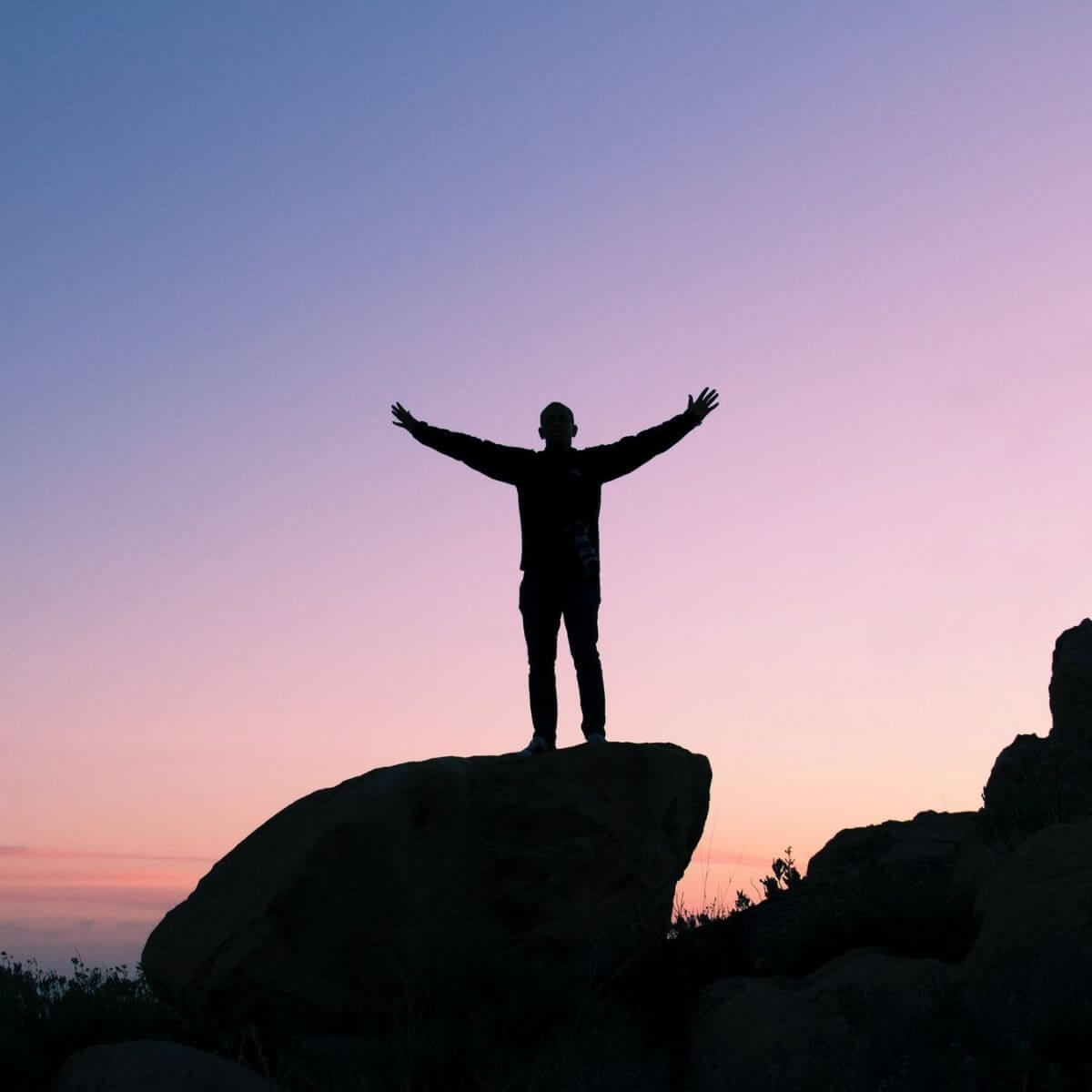 Silhouette of a person standing on a cliff with purple skies.