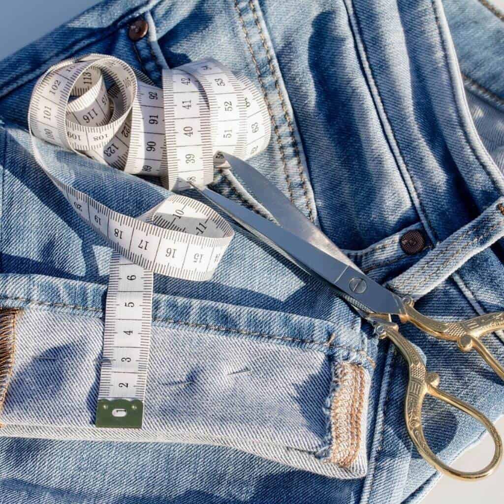 Tape measure and scissors on a pair of jeans with the cuff rolled.
