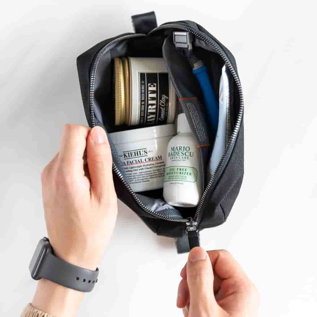 Hands opening a dopp kit with skincare products inside.