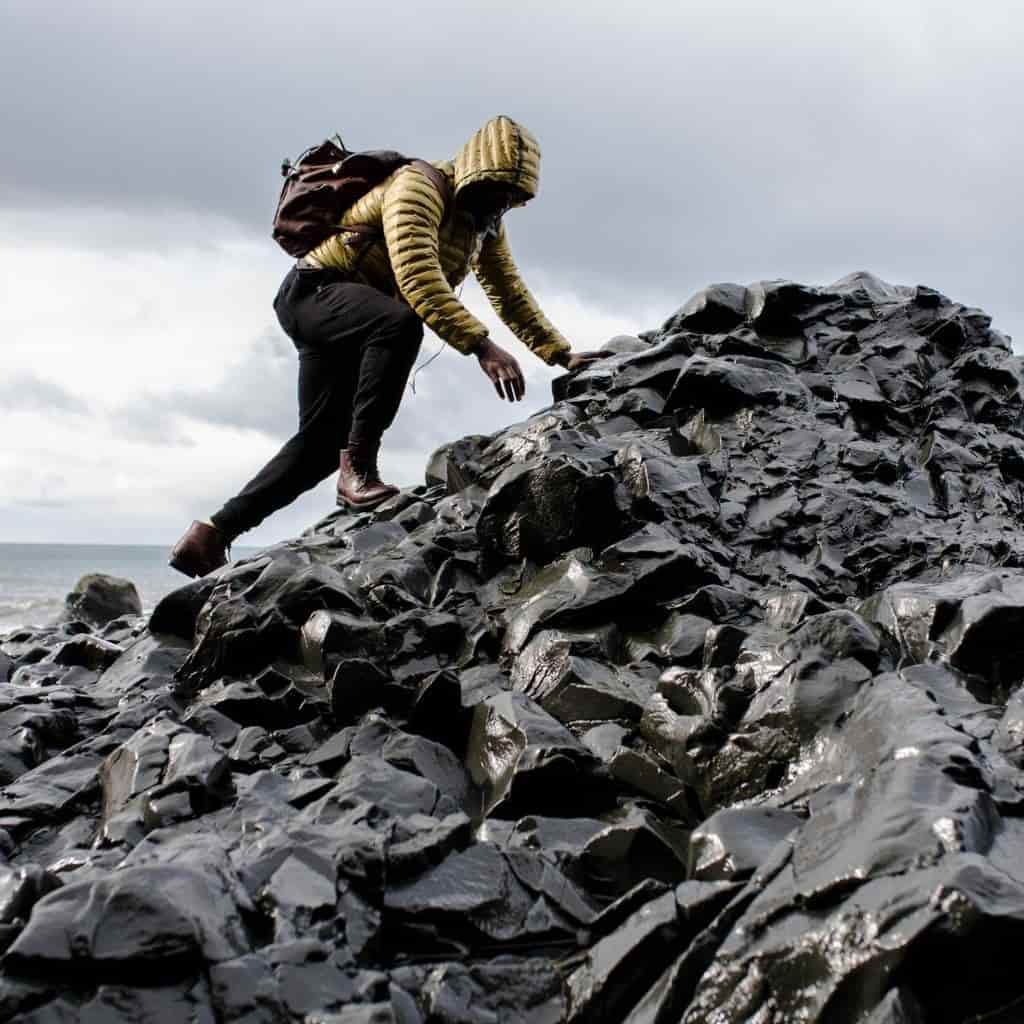 Person climbing rocks in front of an ocean in the rain.