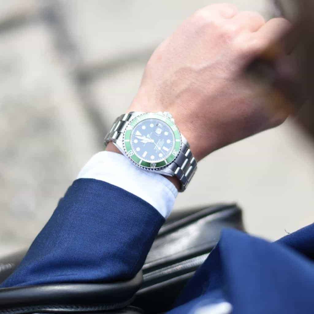 Person wearing a suit and looking down at their Rolex watch.