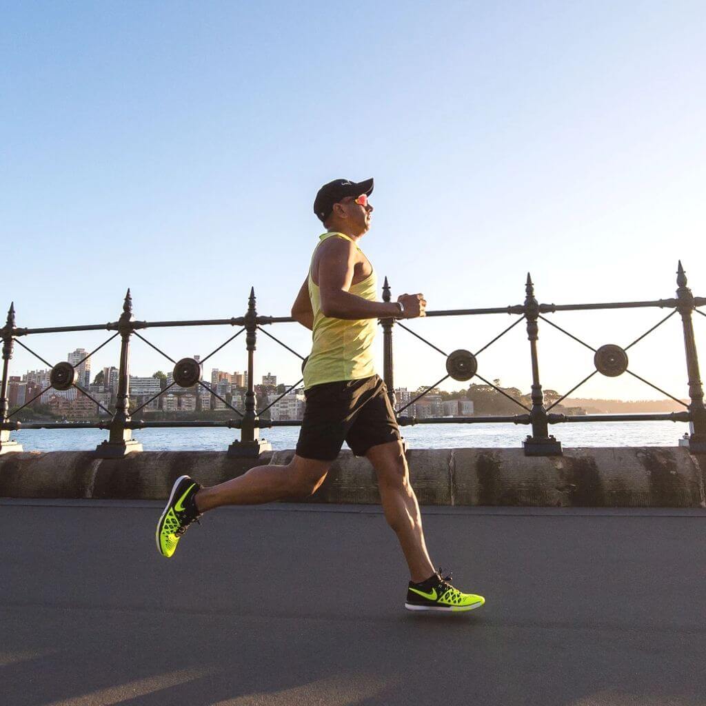 Person running on a sidewalk next to a river with buildings in the background.