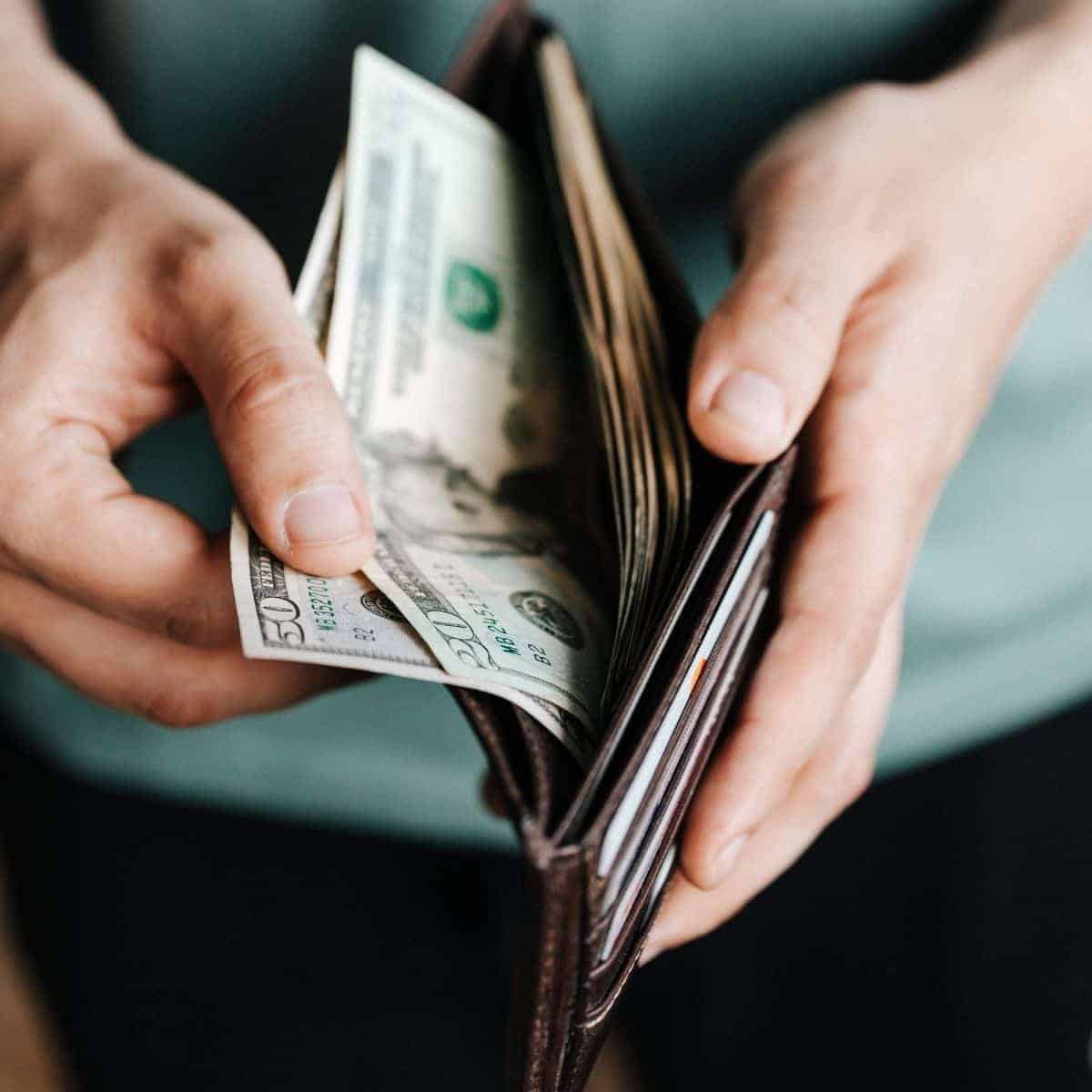 Close-up of a person opening their wallet and grabbing cash.