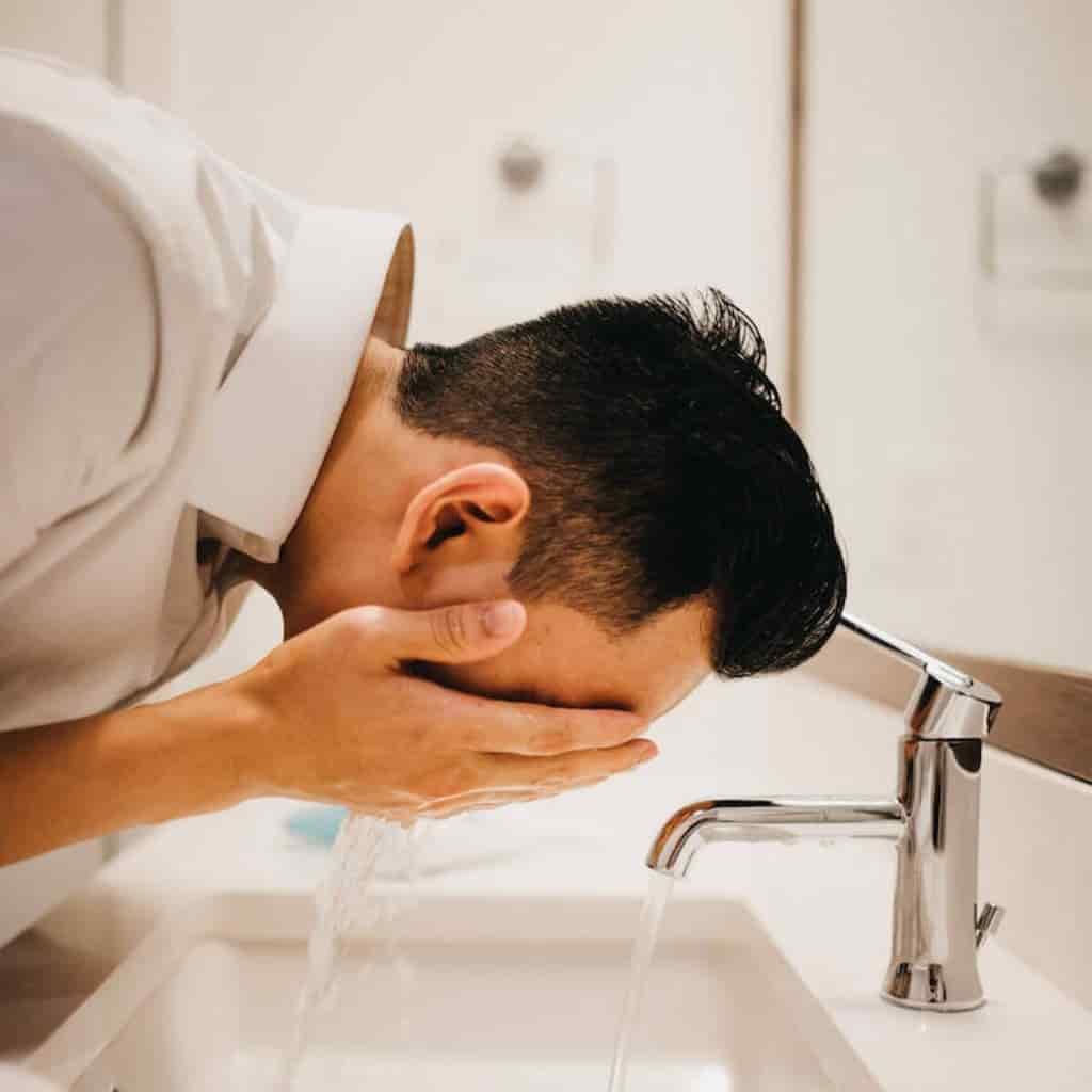 Person washing their face in the sink.