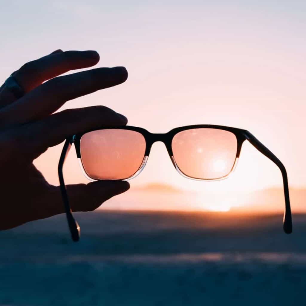 Close-up of a persons hand holding sunglasses up to a sunset.