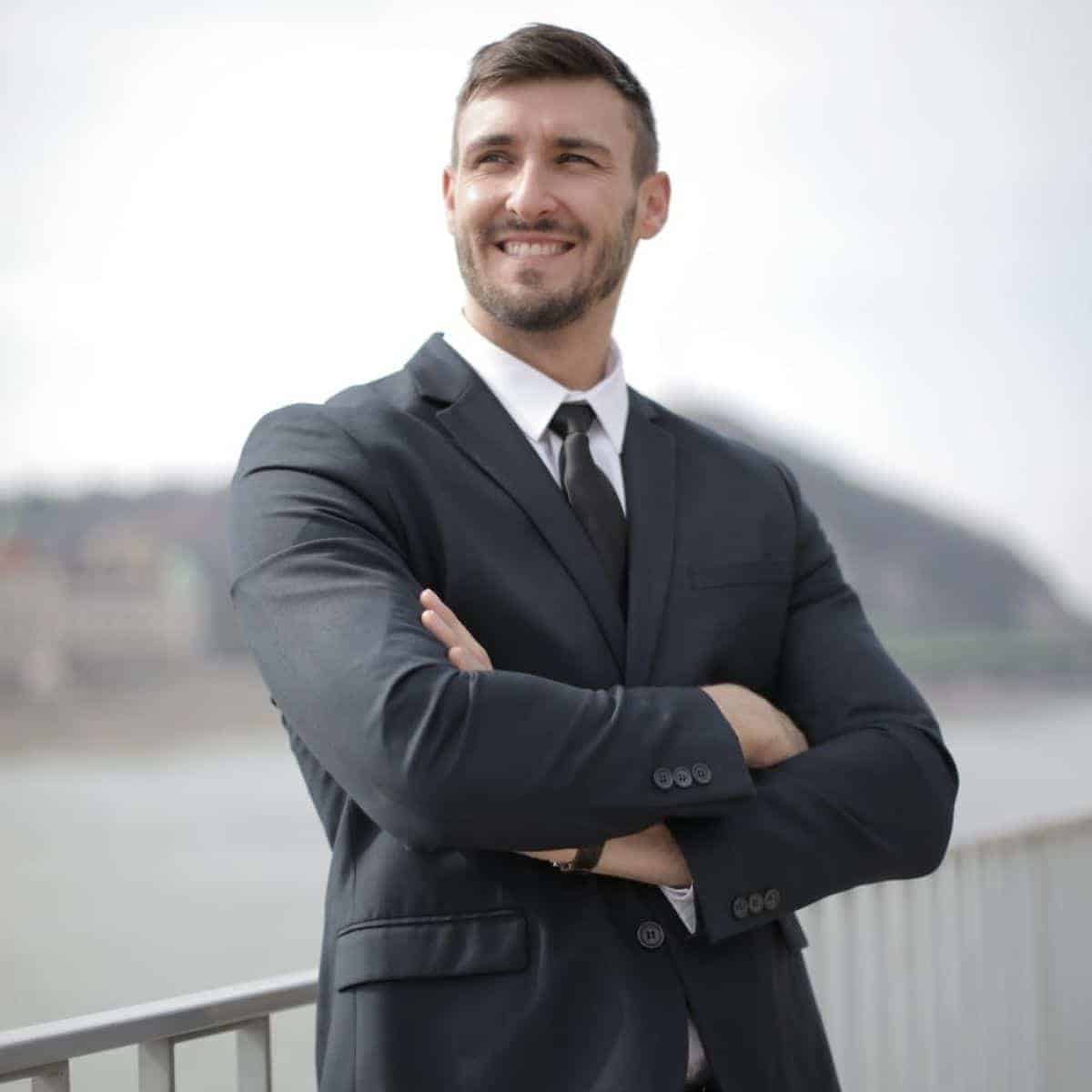 Person wearing a suit and smiling while leaning against a railing.