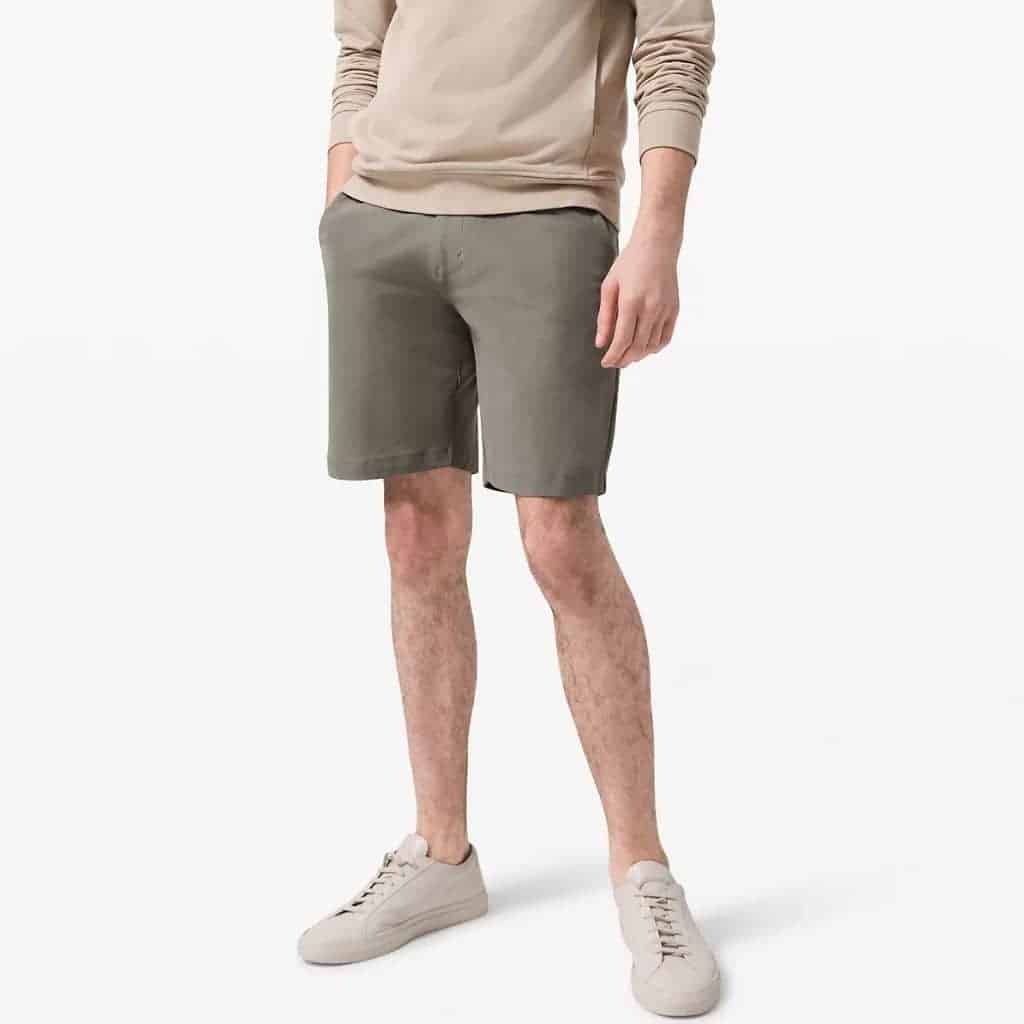 Lower half of a person wearing grey sage shorts and sneakers.