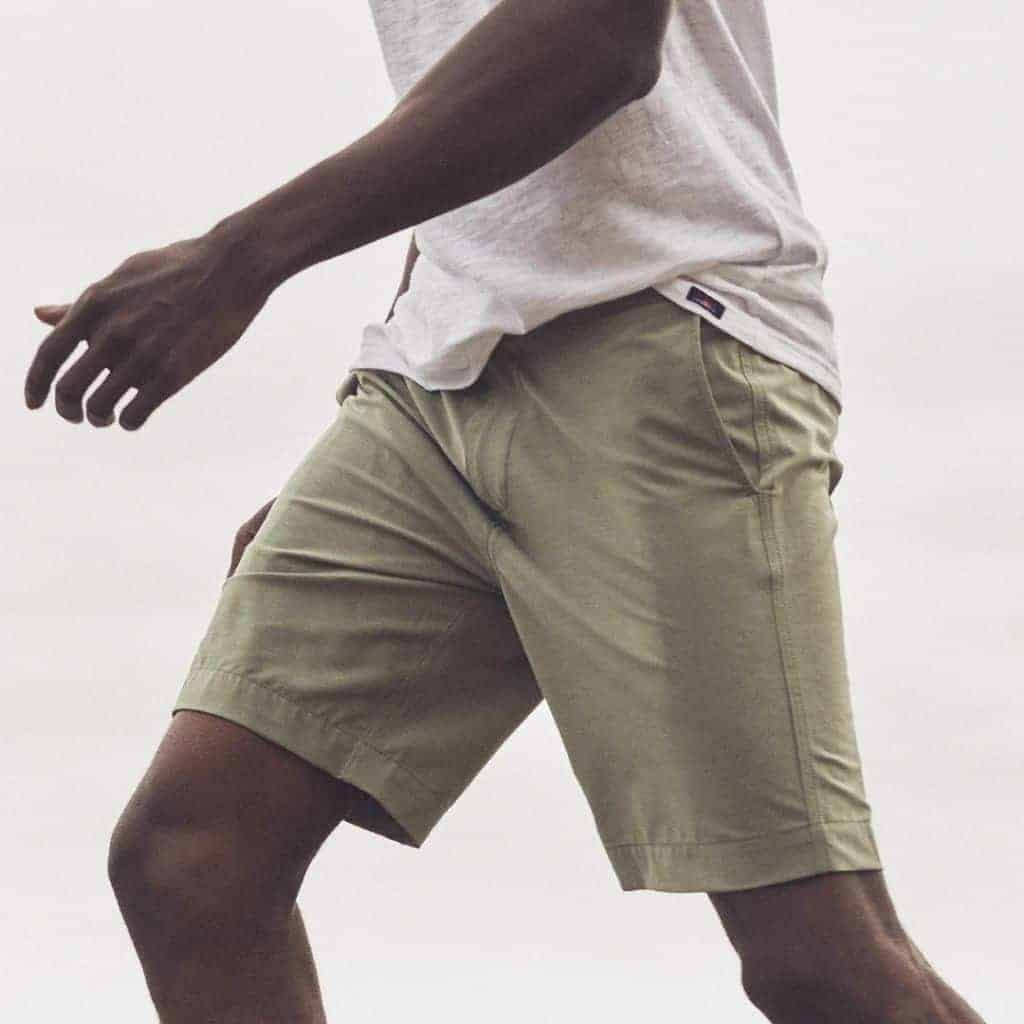 Side view of a person walking with olive shorts and a grey shirt.