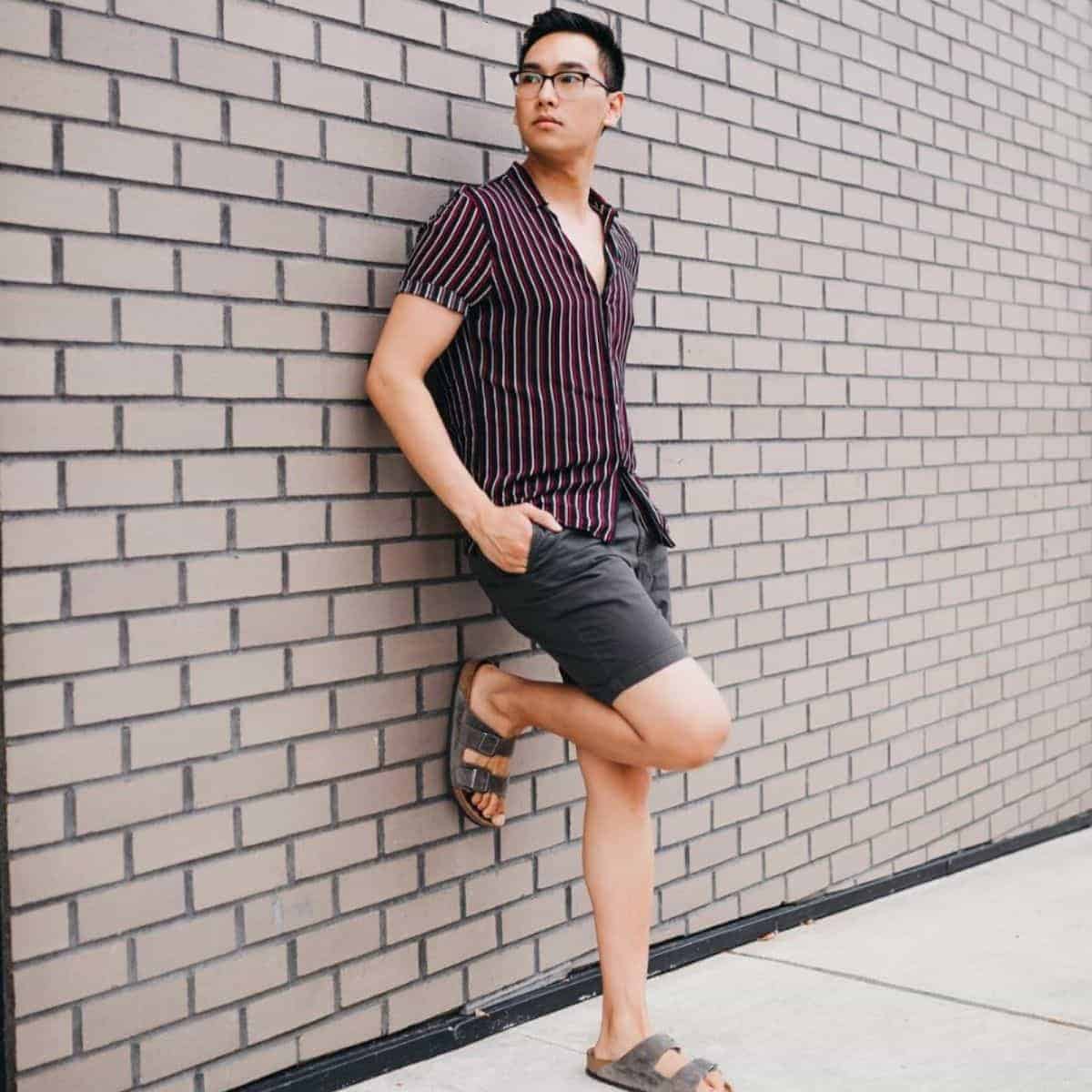 Person wearing shorts and leaning against a brick wall.