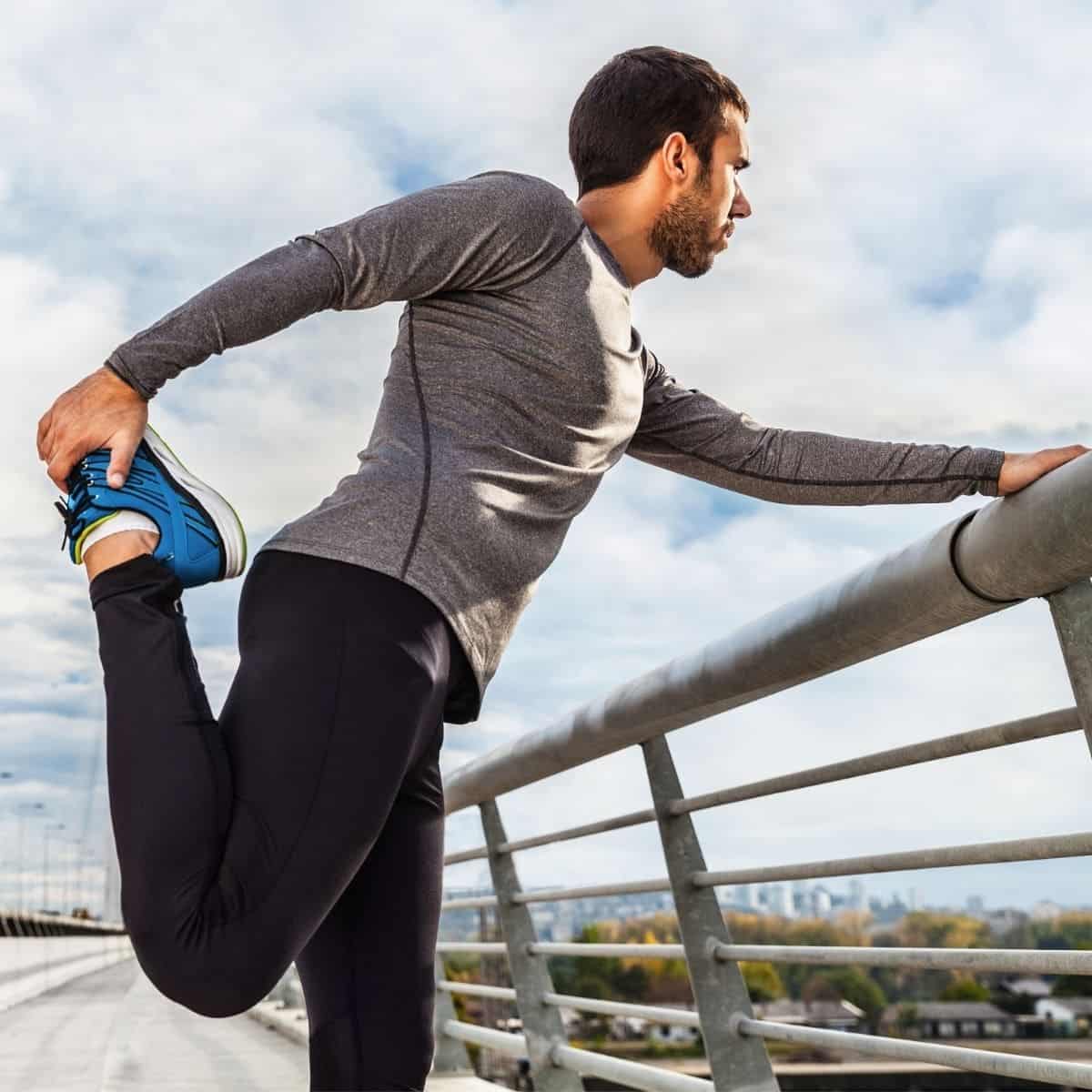 Close-up of a person stretching while holding a railing outside.