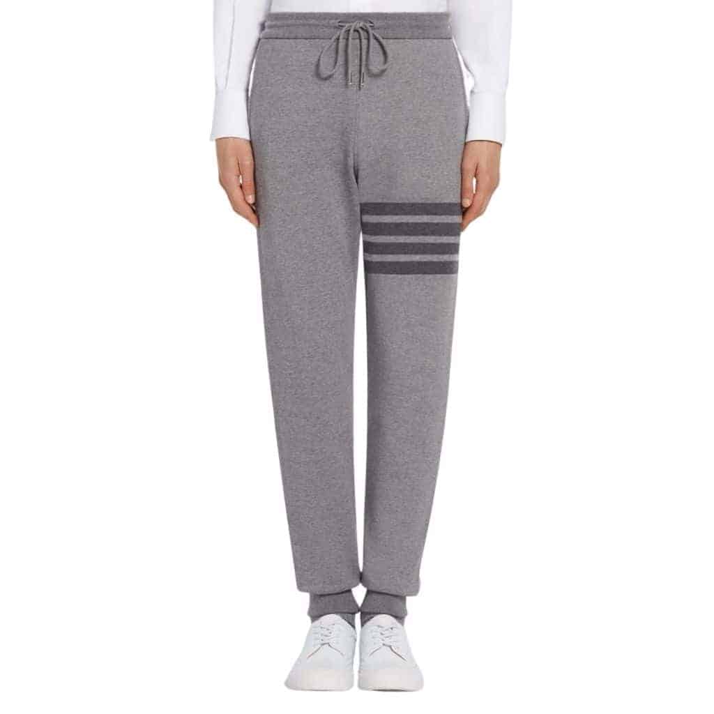 Lower half of a person wearing grey Thom Browne sweatpants.