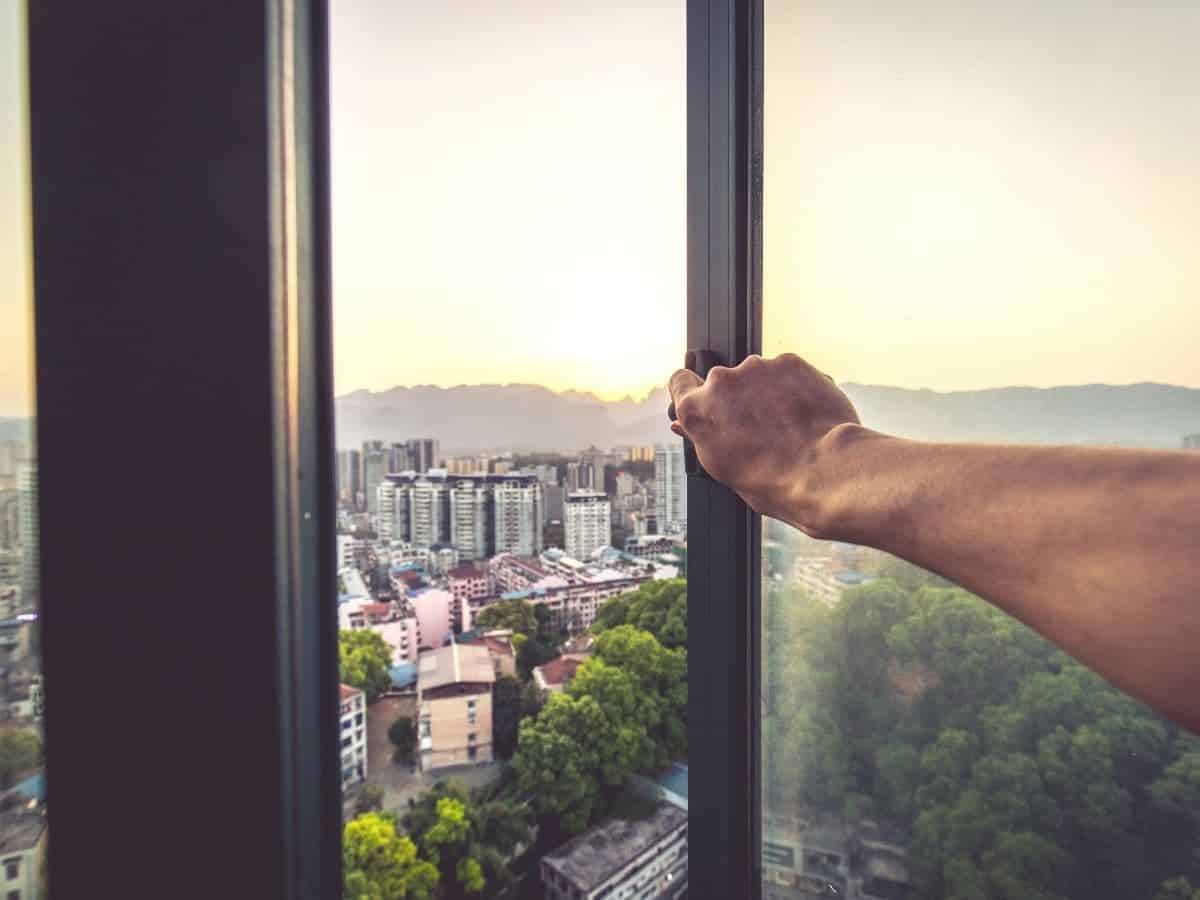 Arm opening a window with a view of the city.