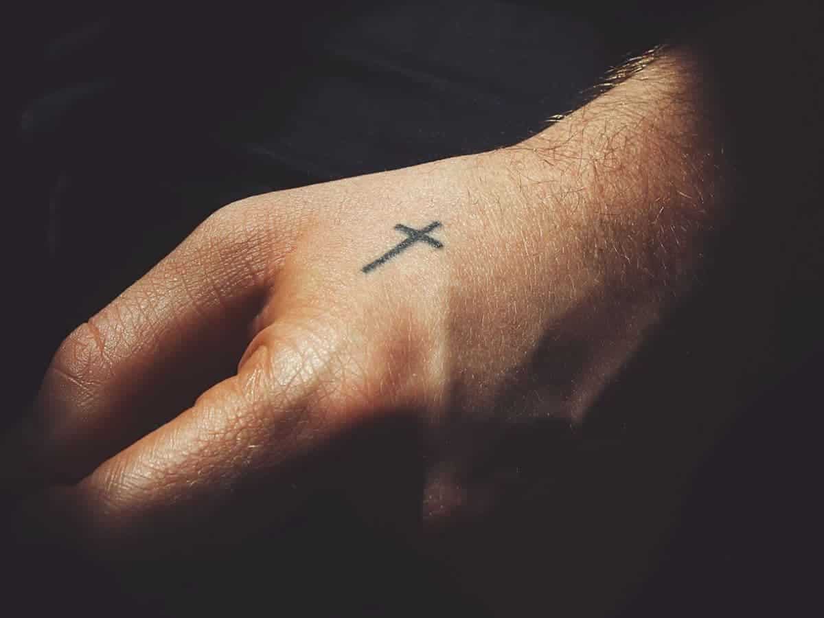 Cross tattoo on a person's hand.