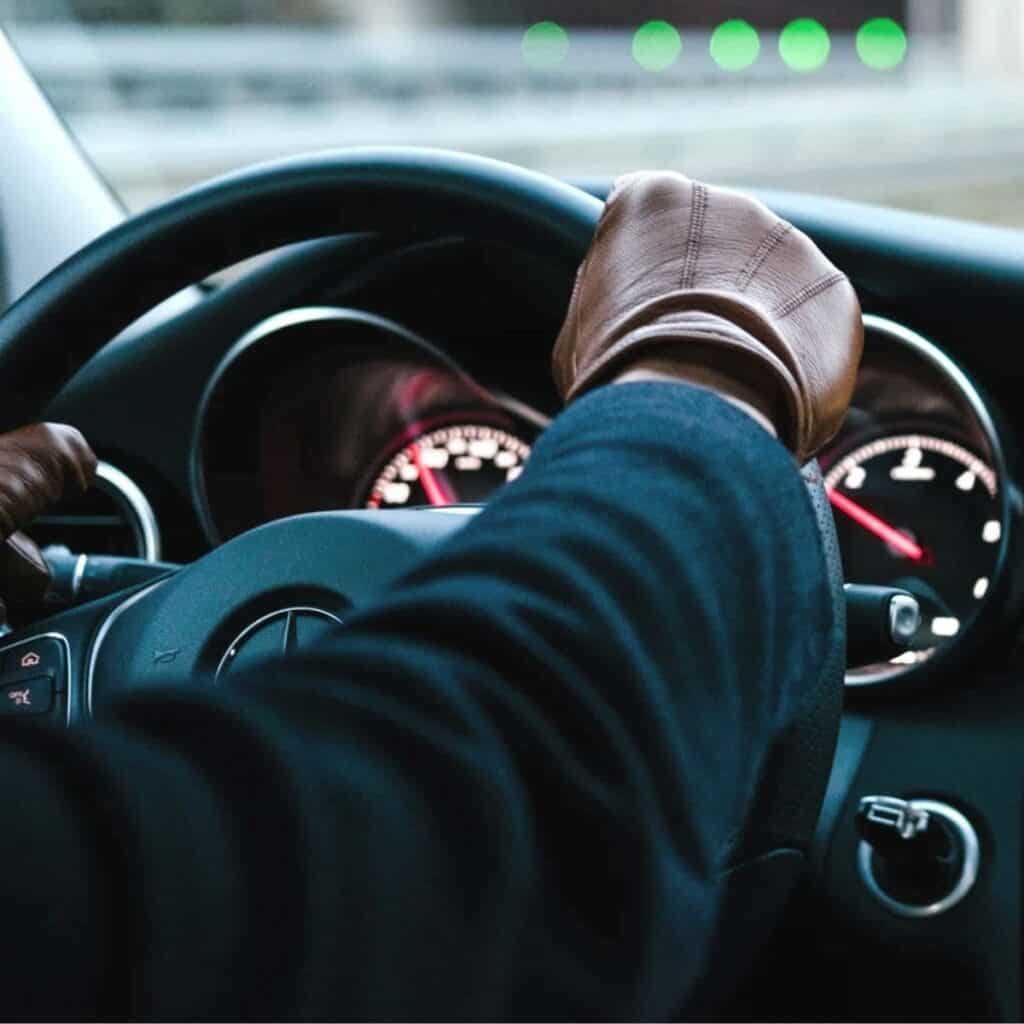 Person wearing leather driving gloves and holding a steering wheel.