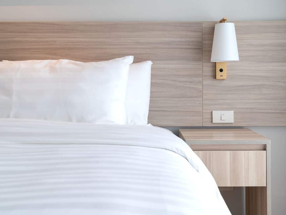 Nicely made bed and wooden bedside table.