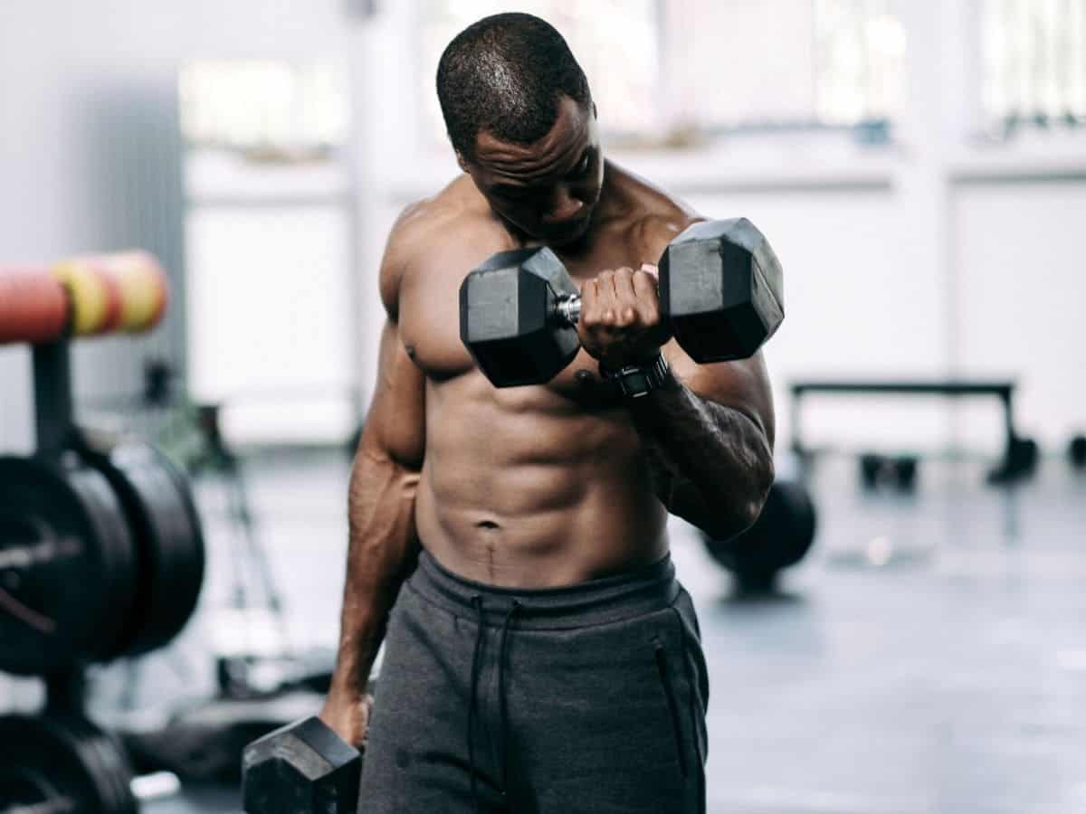 Shirtless person doing dumbbell curls.