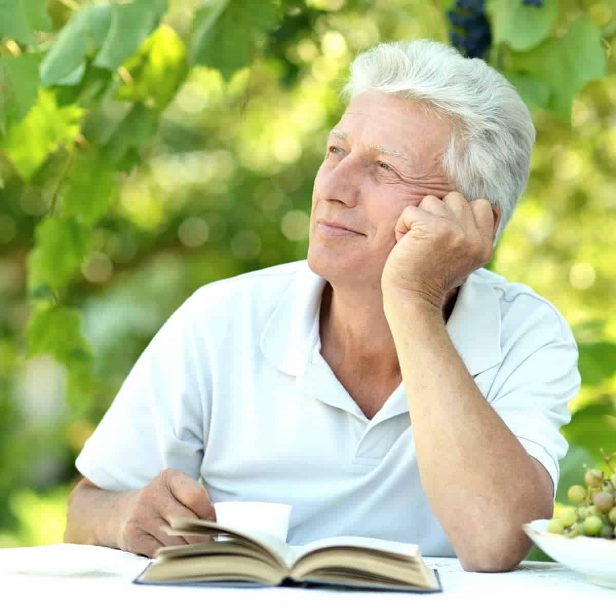Man sitting at a table with a book outdoors and looking to the side.