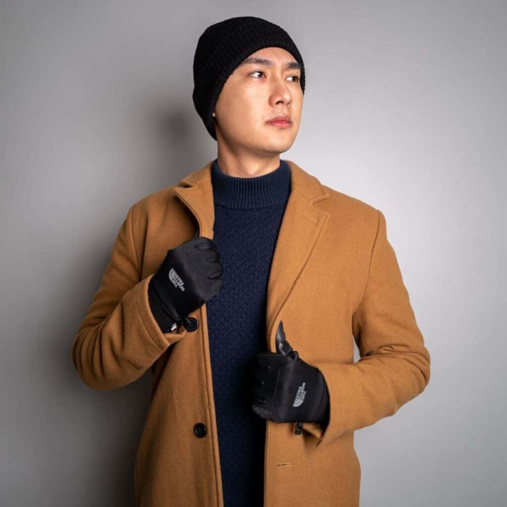 Man wearing a sweater, overcoat, gloves, and a beanie.