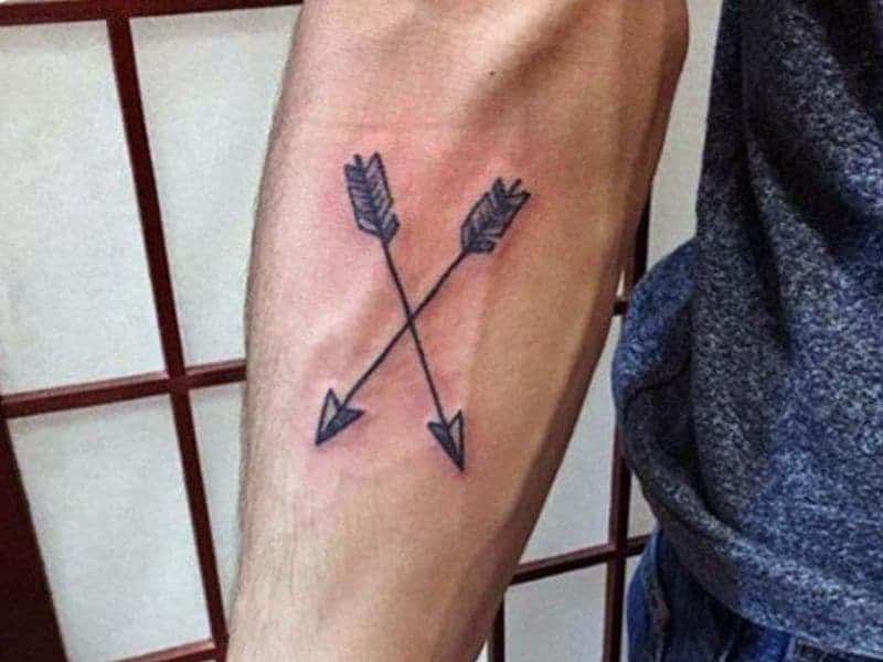 Person's forearm with a crossed arrows tattoo.