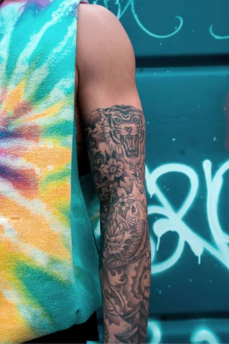 Person's arm with a tattoo of a tiger, flowers, and clouds.