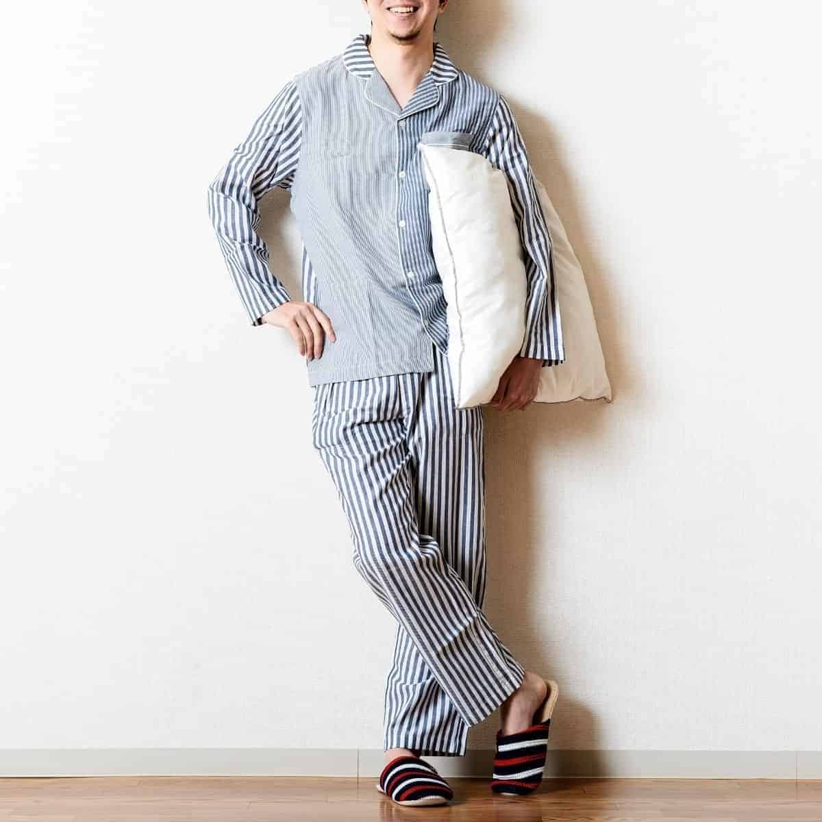 Person wearing pajamas and leaning against a wall with a pillow.