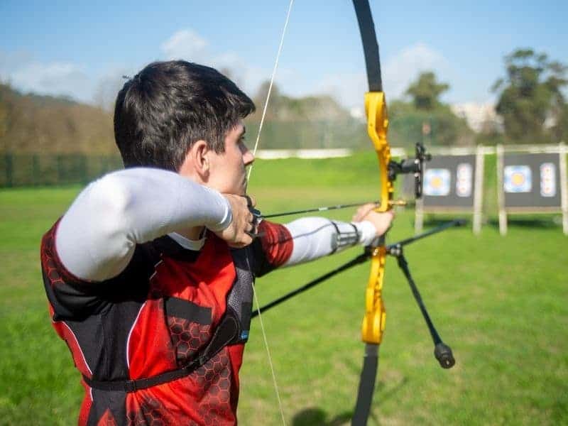 Person holding a bow and arrow and pointing it at an archery target.