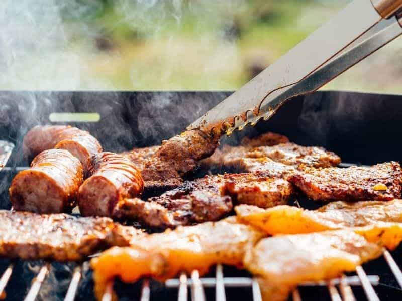 Person using tongs to flip meat on a grill.