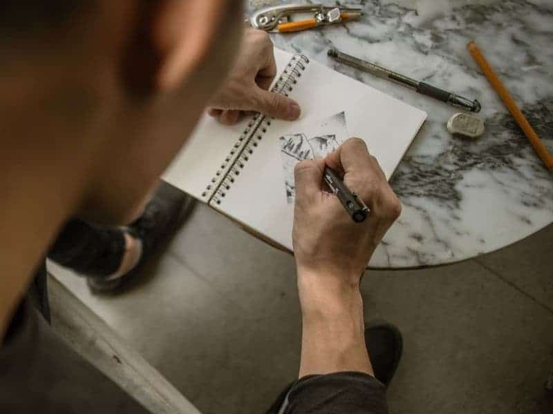 Person drawing with supplies on a table.