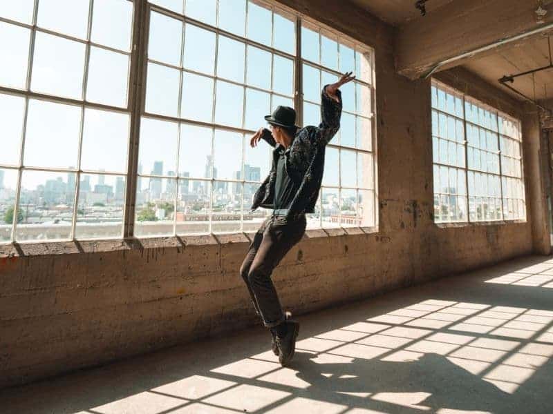Person dancing indoors near large windows.