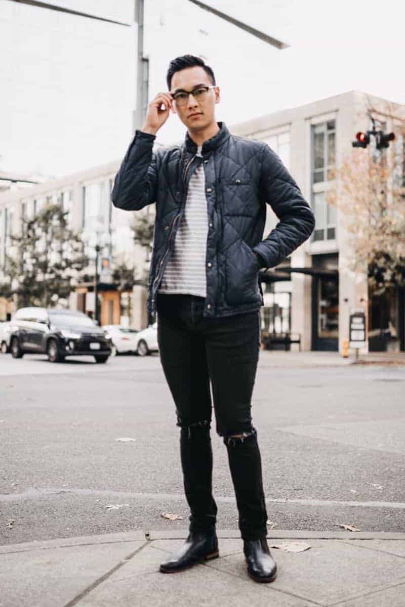 Person standing at the corner of a sidewalk and touching their glasses.