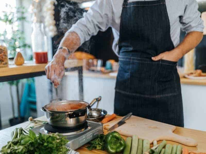 Person wearing an apron and stirring soup.