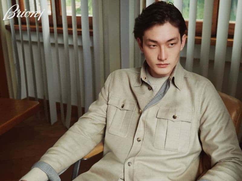 Brioni model wearing an overshirt and sitting in a chair.